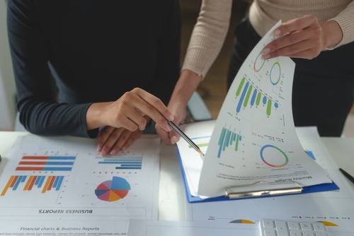 Stock photo, printouts of charts and graphs on a table, with two people interacting with the items on the table