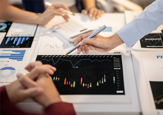 Stock photo, presentation materials with charts and graphs on a table, with multiple hands shown interacting with the items on the table